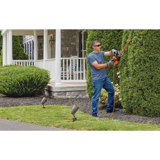 20 in. SAW BLADE Electric Hedge Trimmer being used by person to trim the bushes.