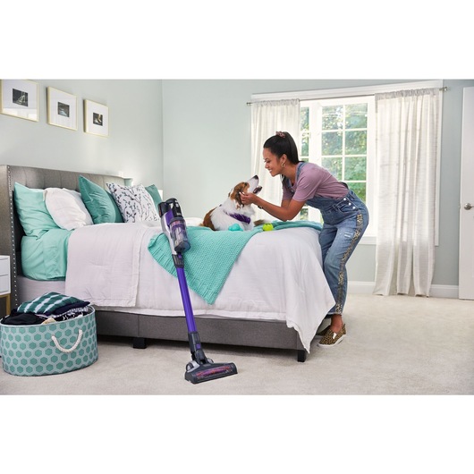 woman petting her dog while taking a break from vacuuming bedroom carpet with BLACK+DECKER PowerseriesExtreme pet stick vacuum