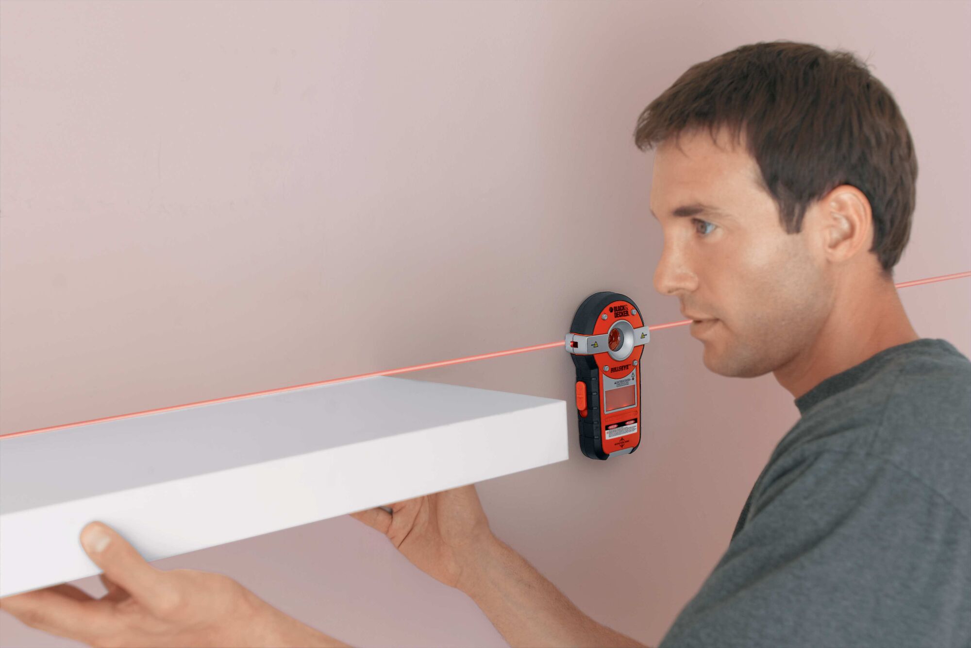 BullsEye auto leveling laser with stud sensor being used by a person to install a shelf.
